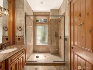 The oversized walk-in shower is beautifully tiled with a frameless glass enclosure, built-in shelving, and natural light streaming through a frosted privacy window.