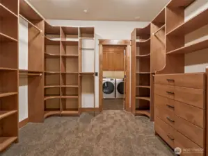 Expansive walk-in closet features a full built-in organization system with open shelving, dual hanging bars, soft-close drawers, and elegant corner display units. Direct access to the laundry room adds seamless everyday convenience.