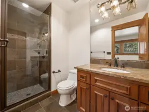 Beautifully tiled ensuite guest bath includes a step-in glass shower, granite countertop, and high-end lighting fixtures. Rich wood cabinetry adds warmth and classic charm to this well-appointed space.
