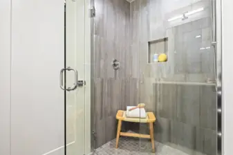 This luxe walk-in shower features oversized tiles and glass doors, a built-in niche, and calming design touches.