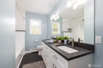 Main floor full guest bathroom has a double vanity of leathered granite, linen closet, and extra storage.  Large bathtub with tile surround.