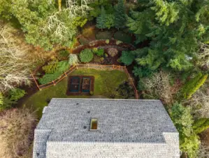 Arial view of the spacious backyard with garden beds fencing and mature landscaping beyond the fence that is also part of the property surrounded by the green belt
