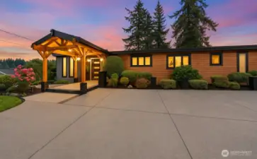 Stunning front elevation showcasing cedar architectural detail, modern lines, and lush landscaping illuminated by the warm glow of sunset