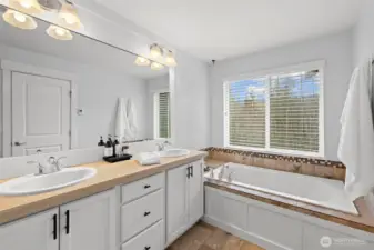 Double vanity with soaking tub looking out to greenspace.