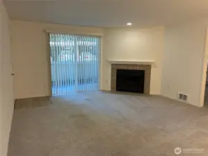 Sunny living room with slider to fenced patio and wood burning fireplace.