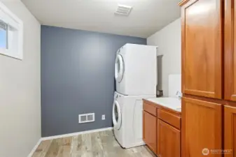 Full-size stacked washer and dryer in spacious utility room with sink and extra storage.