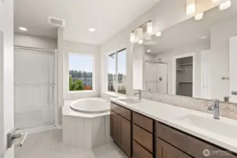 Five-piece primary bath, features dual vanity with quartz counters, tile flooring, and tile deck around deep, soaking tub.