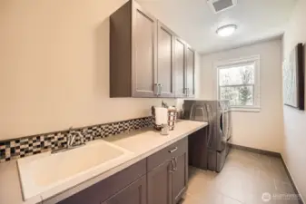 Spacious laundry room with utility sink, ample storage cabinets, designated dirty laundry area, and oversized front-load washer and dryer—offering a functional and efficient space for home upkeep.