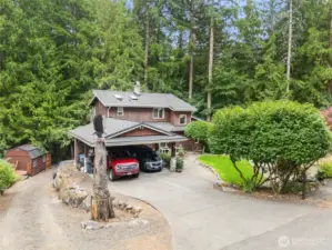 Driveway on the left side leads down to a concrete pad and storage shed.