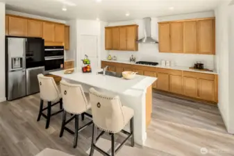 Beautifully finished kitchen featuring a breakfast bar at the center island, stainless steel refrigerator, wall ovens, dishwasher, and lots of cabinet space!