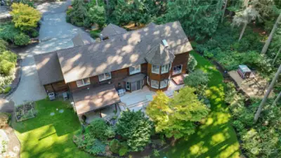 Backyard with an expansive lawn, play structure, chicken coop, raised veggie beds and forest trails.