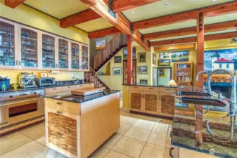 From the elevated kitchen, this view is towards the stairs and entrance to the primary suite. Note the spalted maple cabinet insets, handmade glass cabinet doors and multiple prep sinks.