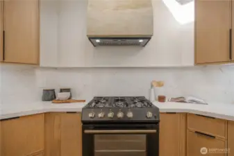 New gas range with venetian plaster hood vent. Spice and sheet pan pull outs flank the range.