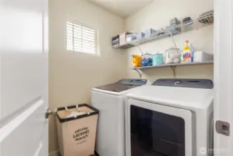 This well-designed upstairs laundry room offers convenience and efficiency, featuring modern appliances and ample storage space. The Samsung washer and dryer are complemented by open shelving, perfect for organizing laundry essentials and keeping everything within easy reach. A large window brings in natural light, making this space bright and inviting. Whether you’re tackling daily chores or doing a quick load, this laundry room is thoughtfully designed to make the task easier and more enjoyable.