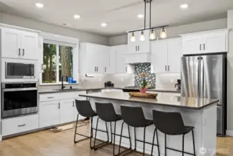 Gourmet kitchen features large island, double ovens, undercabinet lighting, white cabinetry, soft close cabinetry, black fixtures and handles as well as black faucet and black undermount single basin sink.