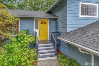 Approaching the entryway, the front steps lead to a covered landing surrounded by vibrant plantings. This welcoming entrance creates a warm first impression for guests.