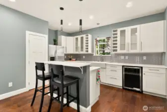 Modern kitchen features a wine fridge, glass cabinetry and a spacious breakfast bar.