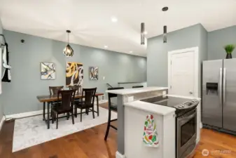 Open-concept layout where the kitchen, dining, and living areas blend beautifully, highlighted by modern lighting, warm wood floors, and stylish finishes throughout. Kitchen with eating space on the large kitchen island, behind the electric stove.