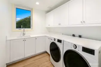 Laundry room with built-in sink, custom cabinetry & countertop including front-loading washer & dryer.