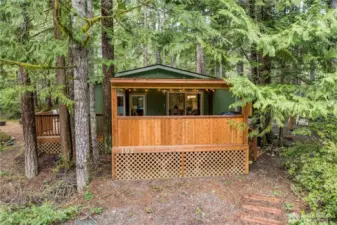 Tucked into the trees, this inviting woodland retreat features a charming front entry with privacy lattice and natural stone steps leading up from a serene garden bench area. Surrounded by lush forest and moss-covered landscaping