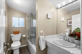 The main-level full bathroom offers sleek glass shower doors and a soothing tub, ideal for unwinding and soaking away your troubles on a chilly, rainy evening.
