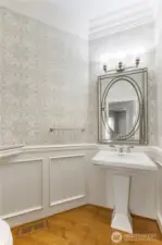 The guest bathroom features a pedestal sink, wood flooring, wainscoting and more.