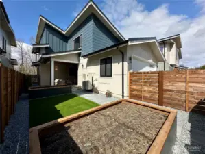 View of the fenced back yard featuring turf lawn, and raised bed planters and gate access to the alley.