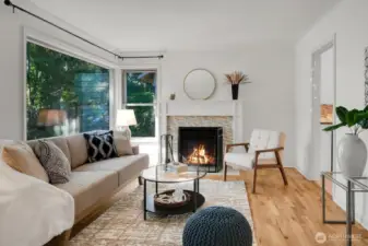 another view of the living room with large picture windows overlooking the front yard and the entryway to the right leading to the kitchen