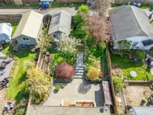 A stunning aerial view of the fully fenced backyard reveals a thoughtfully landscaped garden retreat—complete with tiered stonework, mature trees in full bloom, raised beds, a charming pergola walkway, and plenty of room to relax or entertain in total tranquility.