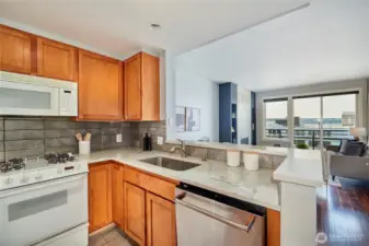 The modern kitchen features quartz counters with full height tile backsplash, under cabinet lighting, undermount sink, tile flooring, a stainless fridge & dishwasher with gas cooking and plenty of storage. Natural gas in included in the monthly HOD's.