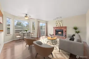 This inviting family room features a classic wood-burning fireplace framed in brick, creating a warm and welcoming focal point. Large windows and a sliding glass door fill the space with natural light and provide easy access to the exterior deck for seamless indoor-outdoor living.