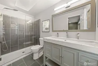 The beautifully updated primary suite bath showcases a sleek double-sink vanity with a marble countertop and modern fixtures. A spacious glass-enclosed shower with full-height tile surround adds a spa-like touch, creating a serene retreat for daily relaxation.