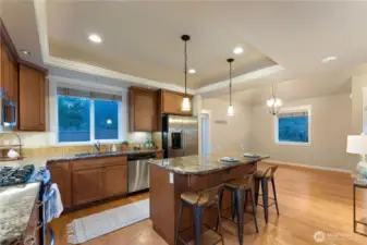 Spacious kitchen with stainless steel appliances, travertine backsplash, granite countertops, and a large island designed for gathering, highlighted by a coffered ceiling.