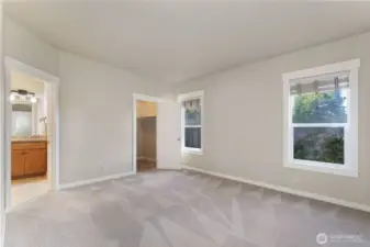 Main-floor primary bedroom featuring windows overlooking the private backyard with convenient access to the five-piece ensuite bath and walk-in closet. Photo depicts the room without furniture; seller furnishings are currently in the home.