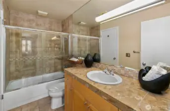 Spa like bath with marble counters, matching maple cabinets, and ceramic shower surround and tiled floors.