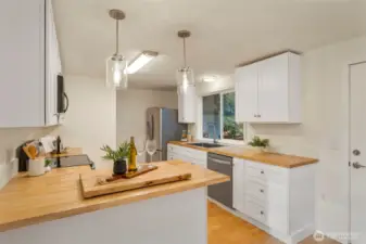 Inviting kitchen has butcher block counters, stainless appliances, and new white cabinets.