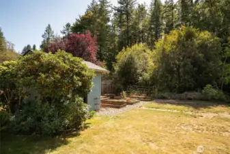 A lovely storage shed and raised garden boxes are framed by mature landscaping, creating a beautiful and practical backyard retreat.