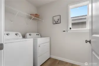 Upper-level laundry room with side-by-side washer/dryer and storage shelf.