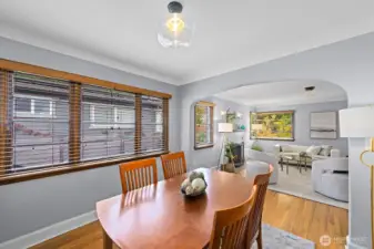 Bright dining area with rich hardwood floors and classic arched entryway opening to cozy living room. Large windows bring in abundant natural light