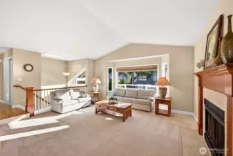 Another angle on the main level living space shows the vaulted ceiling height, the generous window package, and the natural separation created by the split level rail and stair detail. The fireplace adds warmth and a focal point, while the open connection back to the kitchen keeps everyone together. This is the kind of layout buyers appreciate for both quiet nights in and larger gatherings.