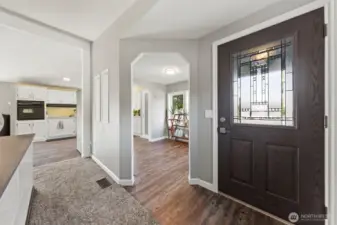 View of entry, formal dining room and kitchen. This shot captures the flow between the entry highlighting the natural light and connection between the spaces.