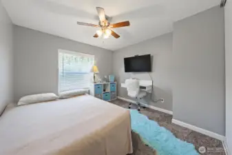 This well-lit second bedroom features an airy atmosphere and a ceiling fan.