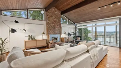 Enjoy a spectacular water view from the comfort of the living room w/vaulted ceiling & large windows, brick wood-burning fireplace and floor to ceiling glass sliders.