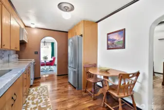 Galley kitchen with space for breakfast table. Stainless Fridge with bottom drawer freezer situated across from stove/range with cabinetry above. Arched entry out to the dining room at end and off to the right is one of the bedrooms.