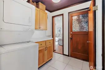 Utility room with stacked laundry machine in between main house and extension/rec room in back. Tile floor with storage cabinets and working countertop space.