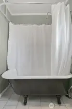 Clawfoot tub with wrap around shower curtain rod and over hanging showerhead. Tile floors.