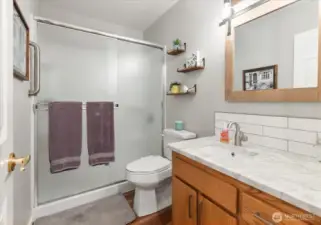 Bathroom with glass-enclosed shower, wood vanity with quartzite countertop, and built-in shelving for storage.