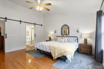 Primary bedroom featuring sliding barn doors leading to the en-suite bath. Hardwood flooring and natural light complete the room.