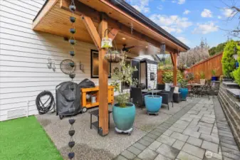 Outdoor living space featuring covered grilling area, seating zones, and decorative planters. Textured concrete and stonework define the layout.
