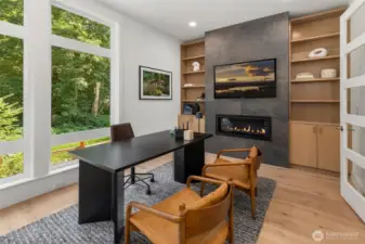 Formal office off of the entry hallway features, glass paneled french doors, wide plank hardwood floors, floor to ceiling tile surround contemporary fireplace, and custom built in cabinets and shelving